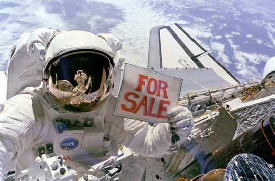 Astronaut Dale A. Gardner holds up a "For Sale" sign refering to two satellites.